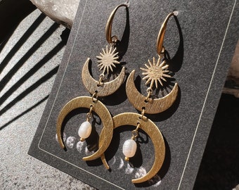 Puede incluir: Pendientes de tono dorado con un diseño de luna creciente y sol. Cada pendiente presenta dos lunas crecientes y un sol con un colgante de perla.