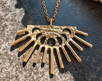 May include: A gold necklace with a sunburst pendant featuring a hammered texture and cut-out crescent moons.