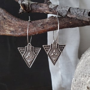 Könnte beinhalten: Ein Paar silberne Creolen mit einem geometrischen Dreiecksanhänger. Das Dreieck hat ein detailliertes Design mit einem Stern in der Mitte.