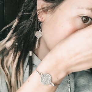 Puede incluir: Una pulsera de plata con un dije de moneda con dise&ntilde;os intrincados. La pulsera se lleva en la mu&ntilde;eca.