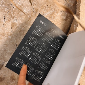Puede incluir: Un calendario en blanco y negro con las fases lunares para cada d&iacute;a del a&ntilde;o 2024. El calendario est&aacute; abierto a los meses de julio y agosto.