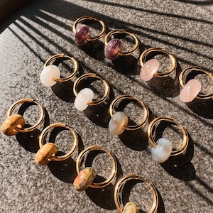 Könnte beinhalten: Eine Sammlung goldener Creolen mit verschiedenen farbigen Steinen. Die Steine sind rosa, lila, weiß und braun.