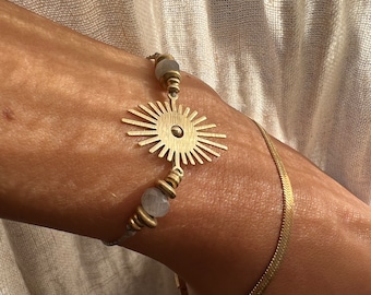 May include: A gold bracelet with a sunburst charm and grey gemstone beads.
