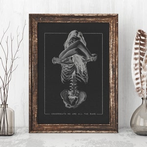 May include: A black and white print of a skeleton with a woman's body superimposed on top. The print is framed in a dark wood frame and the text "UNDERNEATH WE ARE ALL THE SAME" is at the bottom.