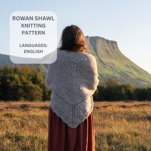 May include: A woman wearing a gray knitted shawl with a delicate lace pattern and a brown skirt, standing in a field with a mountain in the background. The text "ROWAN SHAWL KNITTING PATTERN LANGUAGES: ENGLISH" is visible in the upper left corner of the image.