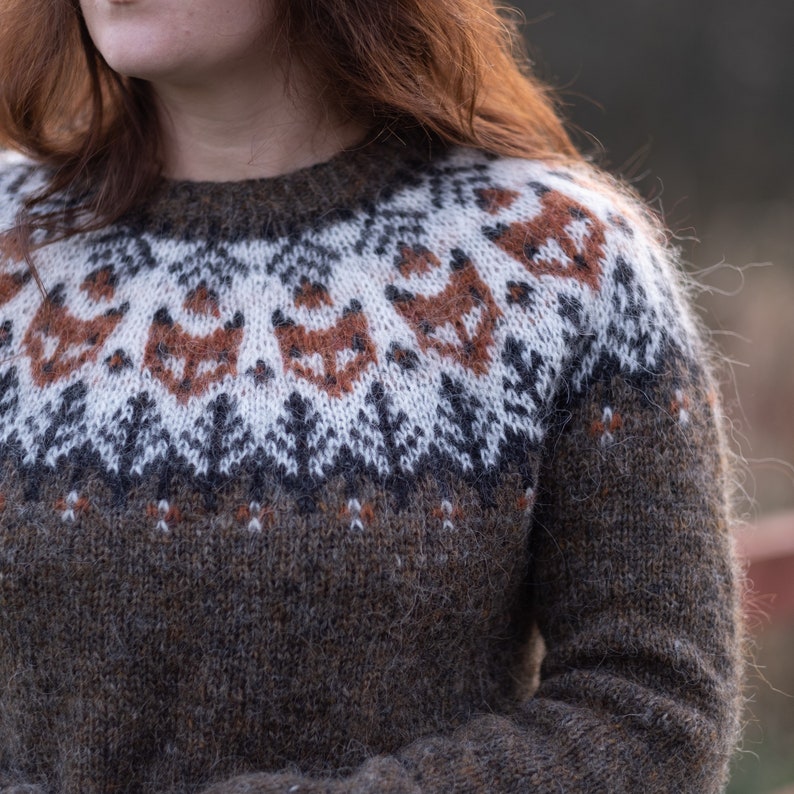May include: A brown, white, and orange knitted sweater with a traditional Scandinavian pattern. The sweater has a crew neck and long sleeves.
