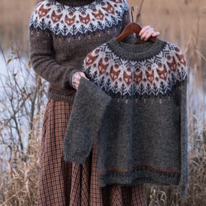 May include: Two knitted sweaters with a fox pattern. The sweater on top is dark green with a brown and white pattern. The sweater underneath is brown with a white and brown pattern. Both sweaters have a fox design.