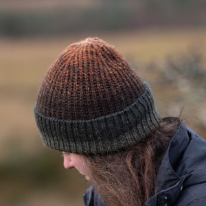 Könnte beinhalten: Eine gestrickte Mütze mit dunkelgrünem Rand und einem Ombre-Muster in Orange, Braun und Schwarz.