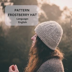 May include: A light beige knitted hat with a textured design, with the text "PATTERN FROSTBERRY HAT Language: English". The hat is worn by a person with long brown hair, set against a blurred outdoor backdrop.