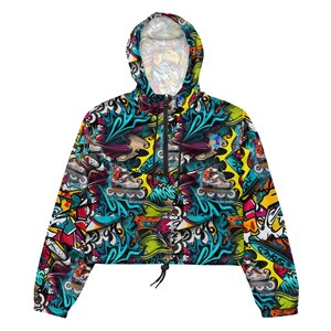 May include: A cropped, hooded jacket with a colourful, graffiti-style print featuring roller skates, flames, and abstract shapes. The jacket has a drawstring at the waist and a zip closure.