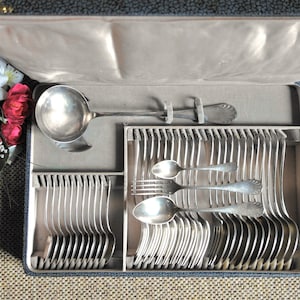 May include: A silver cutlery set in a gray velvet lined case. The set includes a ladle, forks, and spoons.