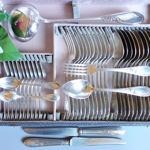 May include: A silver cutlery set in a velvet-lined wooden case. The set includes spoons, forks, and knives, all with ornate handles.
