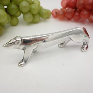 Peut inclure: Un porte-serviettes en argent en forme de chien ou de loup stylisé. Le porte-serviettes est posé sur une surface blanche.