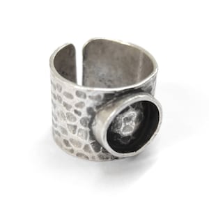 Puede incluir: Un anillo de plata con textura martillada y un engaste redondo. El anillo está abierto en la parte posterior y tiene una banda ancha.