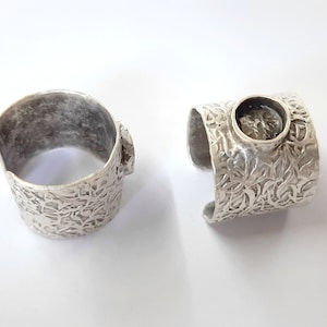 May include: Two silver rings with a textured design. One ring has a round bezel setting for a stone.
