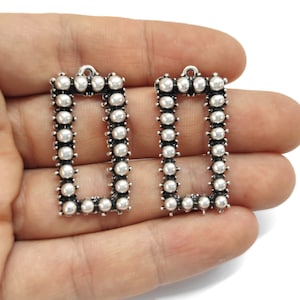 May include: Two silver-toned rectangular earring blanks with a beaded border. The blanks have a loop at the top for attaching earring wires.