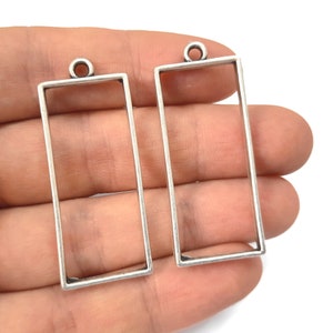 Könnte beinhalten: Zwei rechteckige Rahmen aus silberfarbenem Metall mit einer Öse oben zum Aufhängen. Die Rahmen sind leer und können mit Harz oder anderen Materialien gefüllt werden.