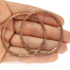 Pode incluir: Dois aros de cobre, um ligeiramente maior que o outro, com uma textura martelada. Os aros estão sobre uma mão, com o aro menor dentro do maior.