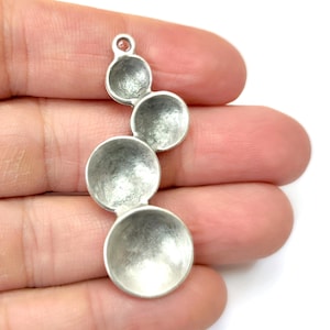 May include: Silver charm with four round, graduated, concave discs. The discs are connected to each other and have a textured surface.
