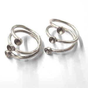 May include: Two silver rings with three round bezels each. The rings are twisted and have a simple design.