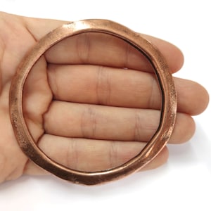 Könnte beinhalten: Ein kupfernes Armreif-Armband mit gehämmerter Oberfläche. Das Armband ist rund und hat eine glatte, polierte Oberfläche.