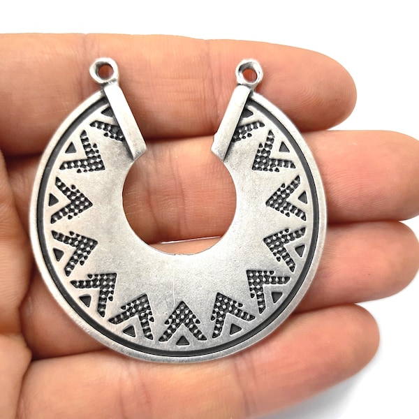 May include: Silver-toned metal pendant with a geometric design. The pendant is shaped like a half-circle with a hole at the top for hanging.