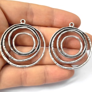 May include: A pair of silver-toned metal earring blanks with a circular design featuring three concentric circles. The circles have a textured, hammered finish.