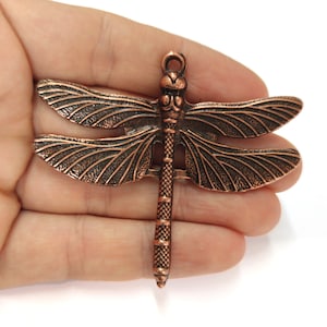 May include: Copper dragonfly charm with detailed wings and a textured body. The charm has a loop at the top for attaching to jewelry or other crafts.