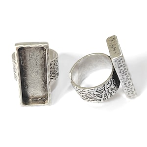 Może przedstawiać: Dwa srebrne pierścionki z prostokątnym oprawą. Pierścionki mają fakturowany wzór.