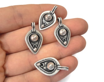 May include: Four silver pendant charms in the shape of a teardrop with a raised circle in the centre and decorative details around the edge.