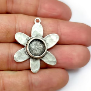 May include: Silver flower charm with a round, open space in the center. The flower has a hammered texture.