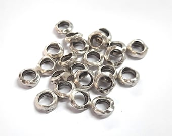 May include: A pile of silver-toned metal rings with a textured finish. The rings are all the same size and shape, and they are arranged in a random pattern.