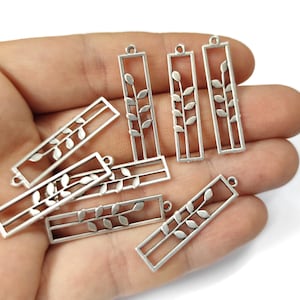 May include: A set of seven silver-toned metal charms featuring a leaf design. The charms are rectangular in shape and have a hole at the top for attaching to jewelry or other crafts.