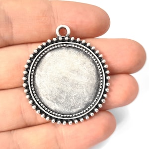 Peut inclure: Pendentif en argent avec une surface ronde, biseautée et vide, et une bordure perlée. Le pendentif a une boucle en haut pour attacher une chaîne.