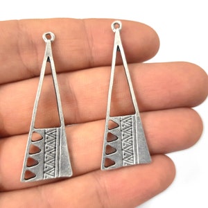 May include: Two silver triangle-shaped earring blanks with a geometric design. The blanks have a hole at the top for attaching earring hooks.