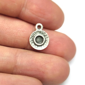 Op de afbeelding: Zilveren bedel met een rond, getextureerd ontwerp en een ronde opening in het midden. De bedel heeft een lus aan de bovenkant om aan een ketting of armband te bevestigen.