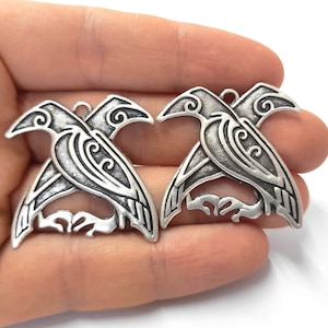 May include: Two silver-toned metal charms in the shape of a stylized raven. The ravens are facing opposite directions and have intricate details.