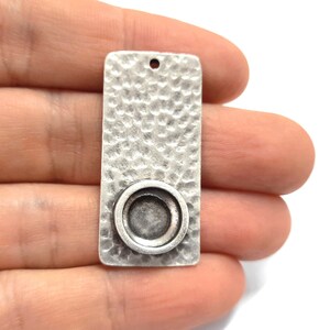 May include: Silver rectangular pendant with a textured surface and a round, recessed area for a cameo or other embellishment.