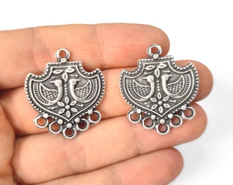 May include: Two silver-toned pendant charms featuring a decorative design of two birds facing each other. The design is surrounded by a floral pattern and has a scalloped edge. Each charm has a loop at the top for attaching to a necklace or bracelet.