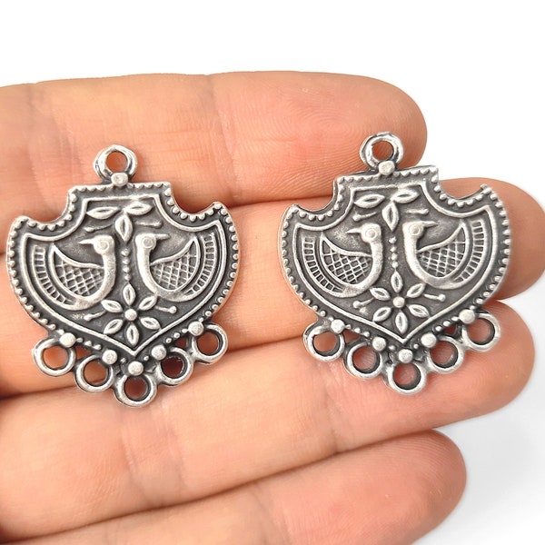 May include: Two silver-toned pendant charms featuring a decorative design of two birds facing each other. The design is surrounded by a floral pattern and has a scalloped edge. Each charm has a loop at the top for attaching to a necklace or bracelet.