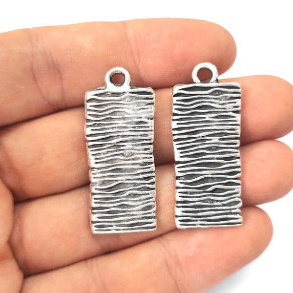 May include: Two silver-toned metal rectangular charms with a textured wavy design. The charms have a loop at the top for attaching to jewellery or other crafts.