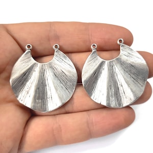 May include: Two silver metal fan-shaped earring charms with a rounded top and a hole on each side for attaching to jewelry.