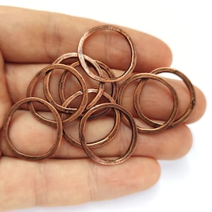May include: A pile of 10 copper jump rings, approximately 1 inch in diameter, in a hand.