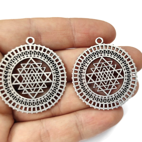 May include: Two silver-toned metal pendants with a geometric design. Each pendant features a circular frame with a detailed pattern and a central star-shaped design.