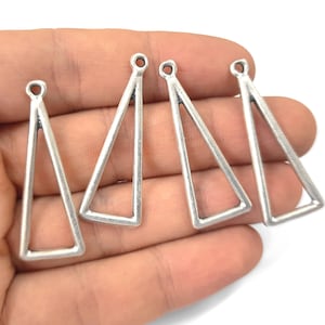 May include: Four silver triangle shaped metal charms with a loop at the top. The charms are hanging from a hand.