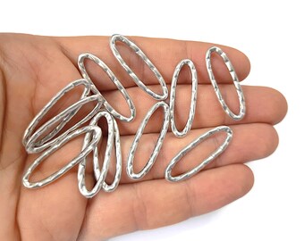 May include: A collection of silver oval-shaped jump rings with a textured finish. The rings are arranged in a pile on a hand.