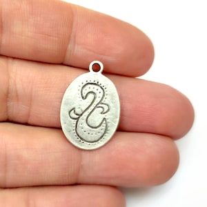 May include: Silver oval charm with a stylized design of a bird or a wave. The charm has a textured surface and a loop at the top for attaching to a necklace or bracelet.