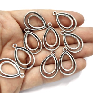 Puede incluir: Diez colgantes de metal de forma de lágrima de color plateado con un diseño de doble anillo. Cada colgante tiene un bucle en la parte superior para sujetarlo a joyas.