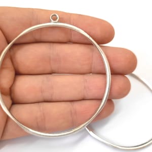 May include: Two silver metal hoops with a loop at the top of one hoop. The hoops are about 3 inches in diameter.