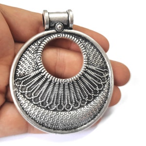 May include: Silver pendant with a circular design featuring a large open circle in the center and intricate details around the edge.